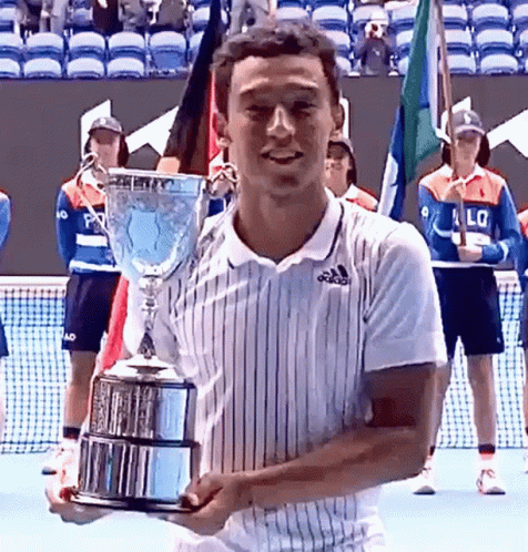A Man In An Adidas Shirt Is Holding A Trophy On A Tennis Court GIF