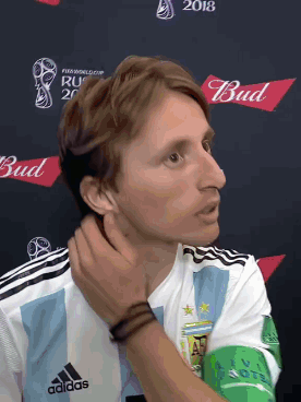 A Man In An Adidas Shirt Is Standing In Front Of A Bud Logo GIF