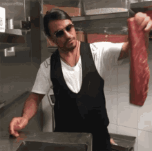 A Man In An Apron Is Holding A Large Piece Of Meat In His Hands . GIF