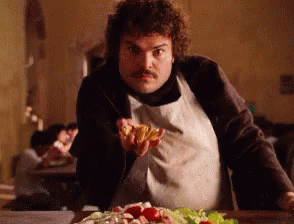 A Man In An Apron Is Holding A Piece Of Pizza In His Hand GIF