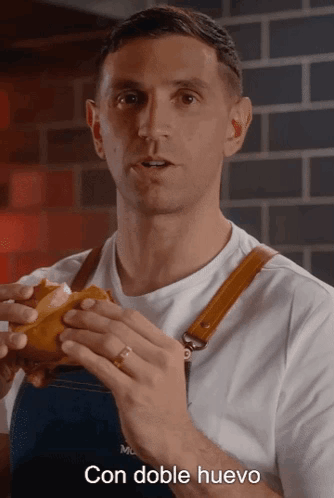 A Man In An Apron Is Holding A Sandwich With The Words Con Doble Huevo Written Below Him GIF