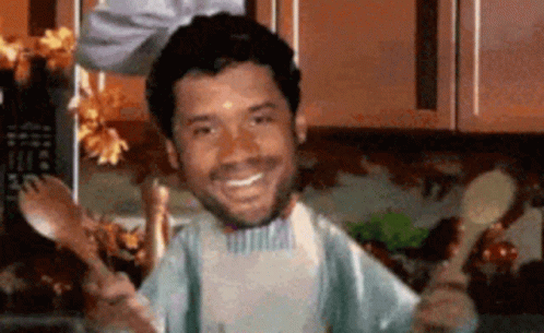 A Man In An Apron Is Holding Spoons And Forks GIF