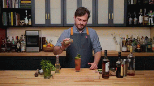 A Man In An Apron Is Preparing A Drink In A Kitchen With Many Bottles GIF