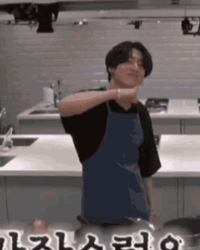 A Man In An Apron Is Standing In A Kitchen With A Pot . GIF