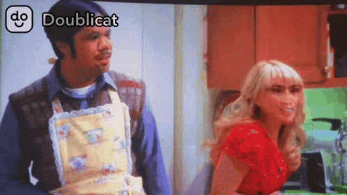 A Man In An Apron Is Standing Next To A Woman In A Red Shirt And The Words Doublicat Are Above Them GIF