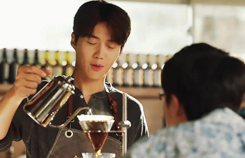 A Man In An Apron Pours Coffee Into A Glass GIF