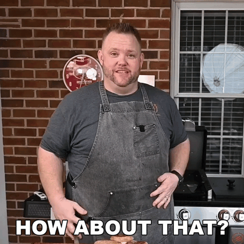 A Man In An Apron Says How About That In Front Of A Brick Wall GIF
