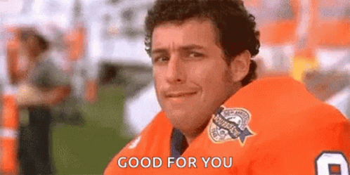 A Man In An Orange Football Jersey Is Sitting On A Bench And Smiling . GIF