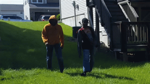 A Man In An Orange Hoodie Walks With Another Man GIF