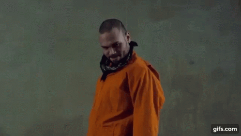 a man in an orange jacket and bandana is standing in front of a wall .