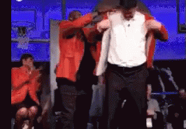 A Man In An Orange Jacket Is Being Lifted By Another Man In A White Shirt GIF