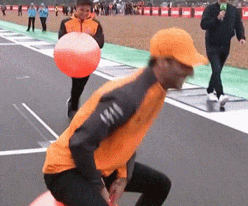 A Man In An Orange Jacket Is Holding An Orange Ball On A Track GIF
