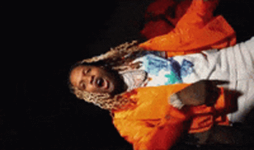 a man in an orange jacket is singing into a microphone in a dark room .