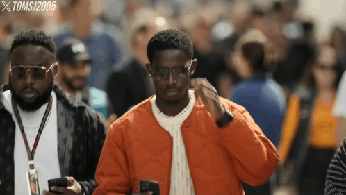 A Man In An Orange Jacket Looks At His Phone While Another Man Looks On GIF