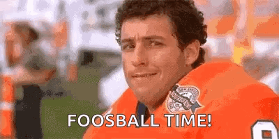 A Man In An Orange Jersey Is Sitting On A Football Field With The Words `` Fooball Time '' Written On His Face . GIF