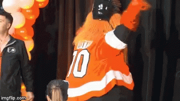 A Man In An Orange Jersey With The Number 10 On It Is Standing In Front Of Balloons . GIF