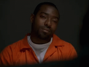 A Man In An Orange Jumpsuit Is Looking Down At Something GIF