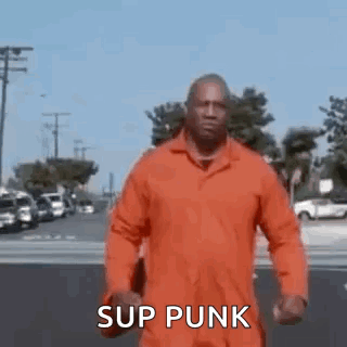 A Man In An Orange Jumpsuit Is Walking Down A Street And Says `` Sup Punk '' . GIF