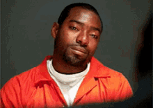 A Man In An Orange Jumpsuit Looks At The Camera With A Serious Look On His Face GIF