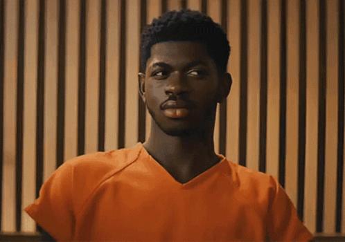 A Man In An Orange Prison Uniform Is Looking At The Camera GIF