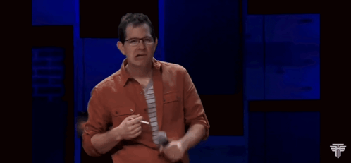 A Man In An Orange Shirt And Tie Is Holding A Microphone In His Hand GIF