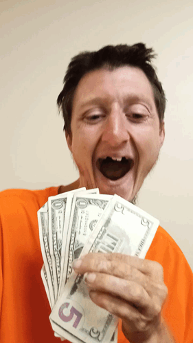 A Man In An Orange Shirt Is Holding A Stack Of 5 Dollar Bills GIF