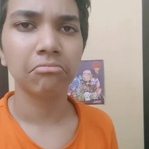 A Man In An Orange Shirt Is Making A Face In Front Of A Poster That Says Ben 10 GIF