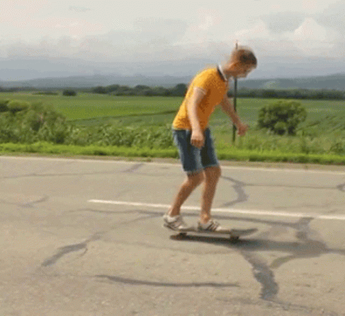 A Man In An Orange Shirt Is Riding A Skateboard Down The Road GIF