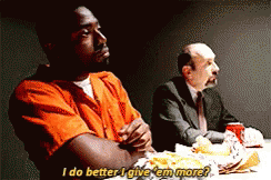 A Man In An Orange Shirt Is Sitting At A Table Talking To Another Man GIF