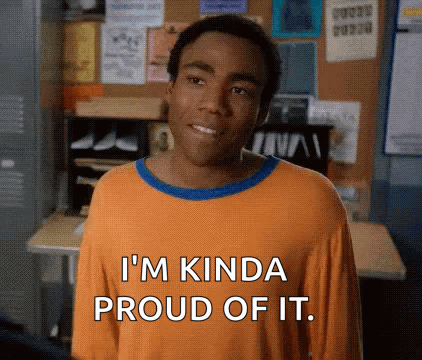 A Man In An Orange Shirt Is Standing In Front Of A Desk And Smiling . GIF