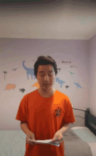 A Man In An Orange Shirt Is Standing In Front Of A Dinosaur Wall Decal GIF