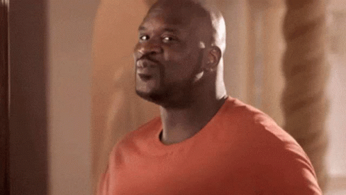 A Man In An Orange Shirt Is Standing In Front Of A Mirror And Making A Funny Face . GIF
