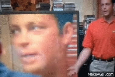 A Man In An Orange Shirt Is Standing In Front Of A Screen With A Picture Of A Man 'S Face On It .. GIF
