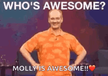 A Man In An Orange Shirt Is Standing On A Stage With His Hands On His Hips And A Heart . GIF