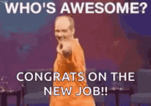 A Man In An Orange Shirt Is Standing On A Stage With His Hands On His Hips And Congratulating Someone On Their New Job . GIF