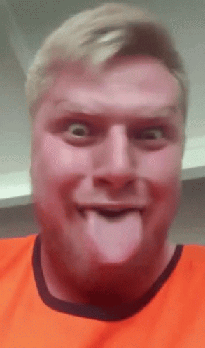 A Man In An Orange Shirt Is Sticking Out His Tongue . GIF