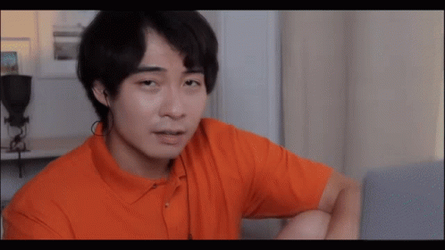 A Man In An Orange Shirt Looks At A Laptop Screen GIF