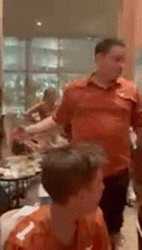 a man in an orange shirt stands in a room with other people