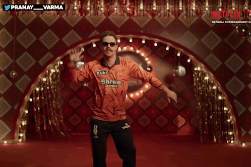 A Man In An Orange Shirt That Says Netflix On It GIF