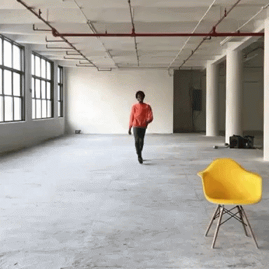 A Man In An Orange Shirt Walks Through An Empty Room GIF