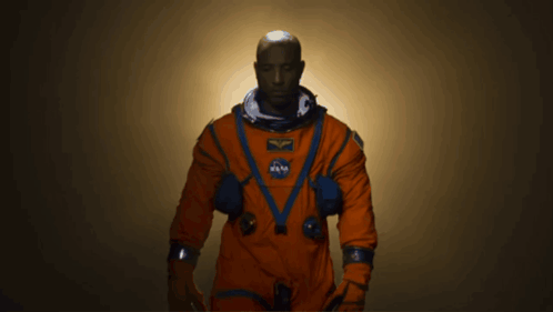 A Man In An Orange Space Suit With A Nasa Patch On His Chest GIF