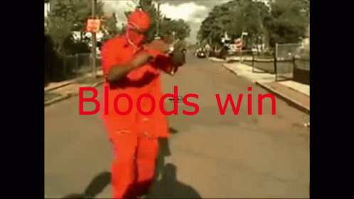 A Man In An Orange Suit Is Walking Down A Street With The Words Bloods Win Written On It GIF