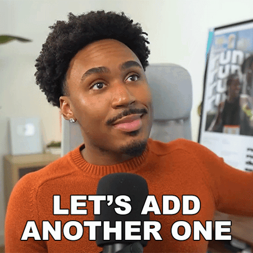 A Man In An Orange Sweater Is Talking Into A Microphone And Says Let 'S Add Another One GIF