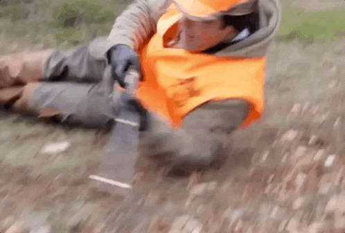 A Man In An Orange Vest Is Laying On The Ground With A Knife . GIF