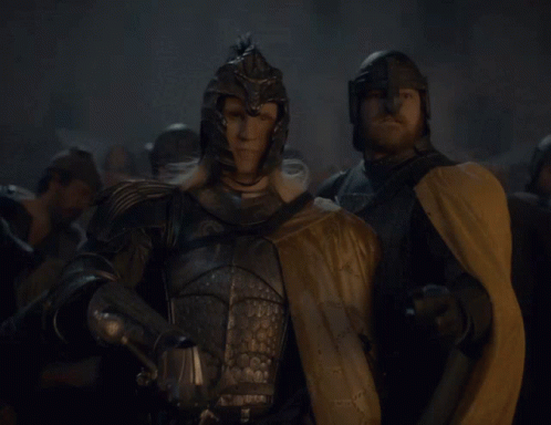 A Man In Armor Holding A Sword Stands Next To Another Man GIF