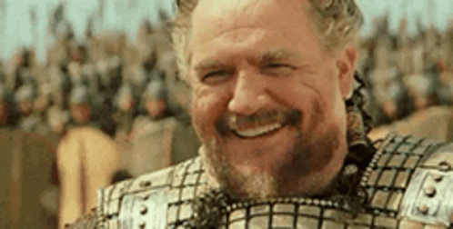 A Man In Armor Is Smiling In Front Of A Crowd Of People . GIF