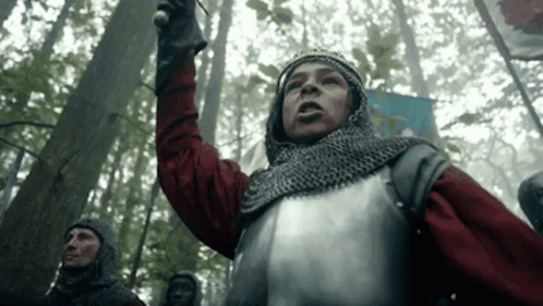 A Man In Armor Is Standing In The Middle Of A Forest Holding A Sword . GIF
