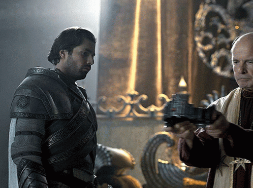 A Man In Armor Is Standing Next To Another Man Who Is Holding A Gun GIF
