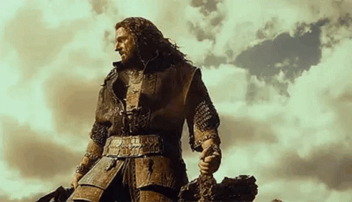 A Man In Armor Is Standing On Top Of A Hill Holding A Sword . GIF