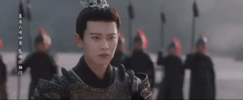 a man in armor with a crown on his head is standing in front of a group of people .